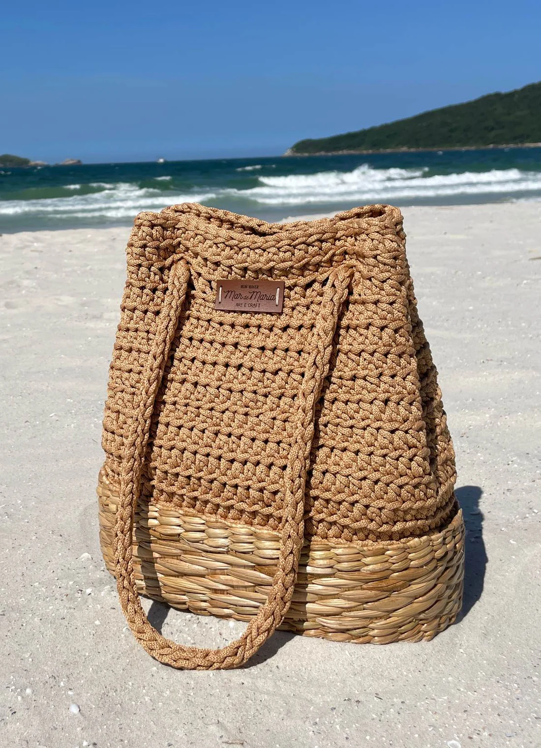 Bolsa de crochê feita com fio de malha natural, apoiada na areia da praia