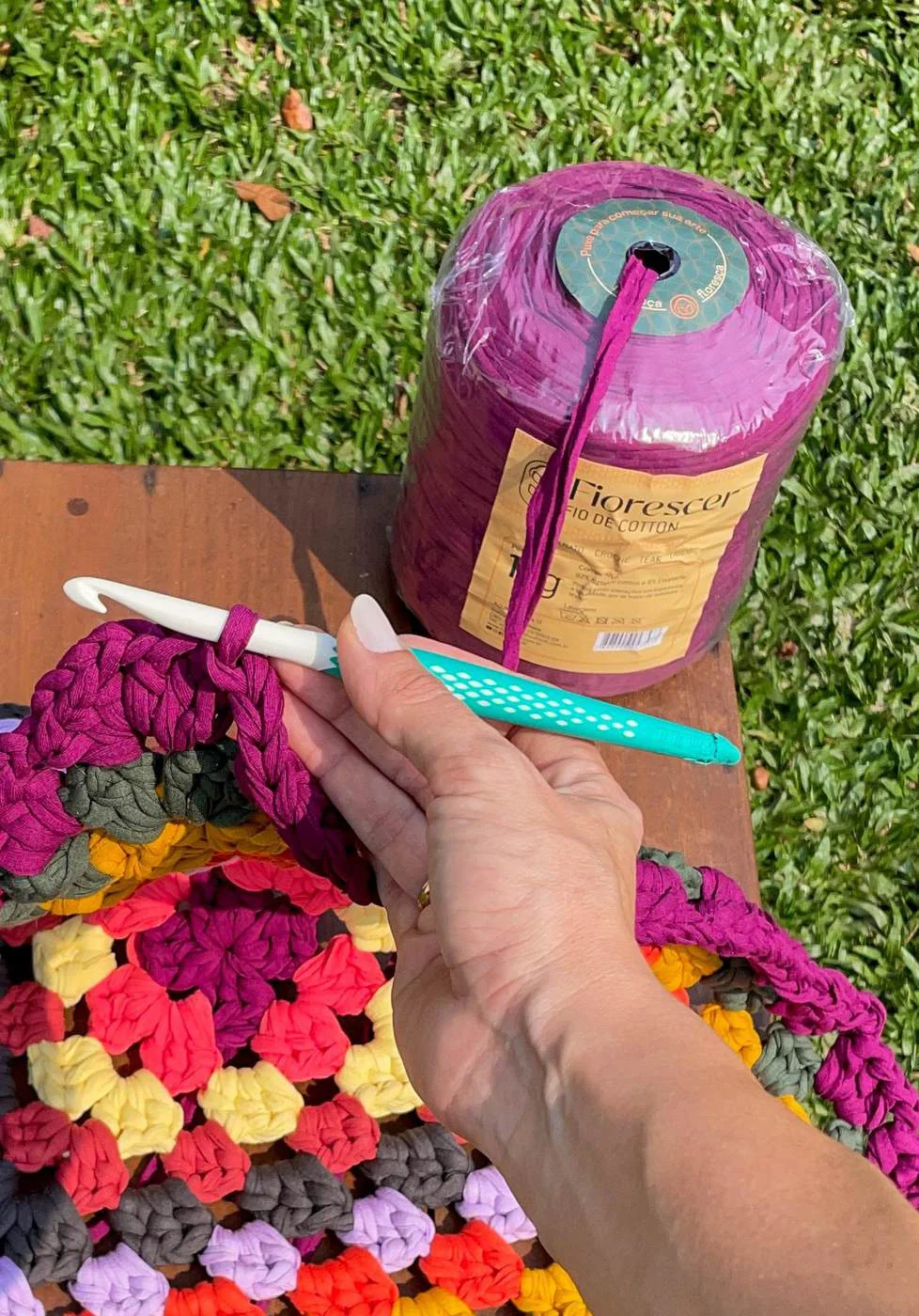 Mãos trabalhando sobre uma manta de crochê formada por dezenas de flores coloridas